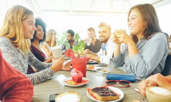Group of adults chatting over a drink and cakes
